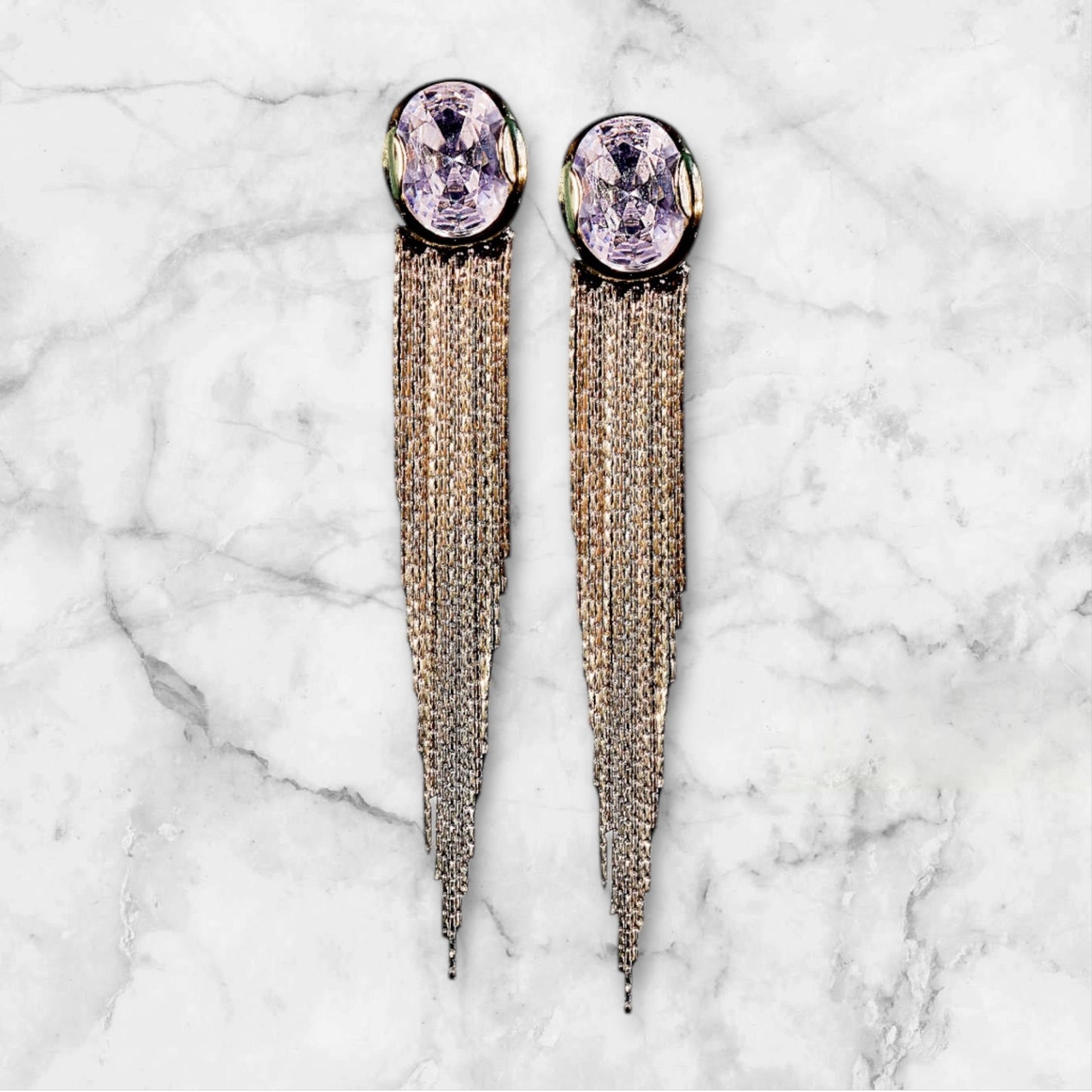 Tassels With Big Crystals earrings feature large pale lavender gems atop cascading silver chain tassels, shown on white marble—a stunning addition to any crystal jewelry collection.