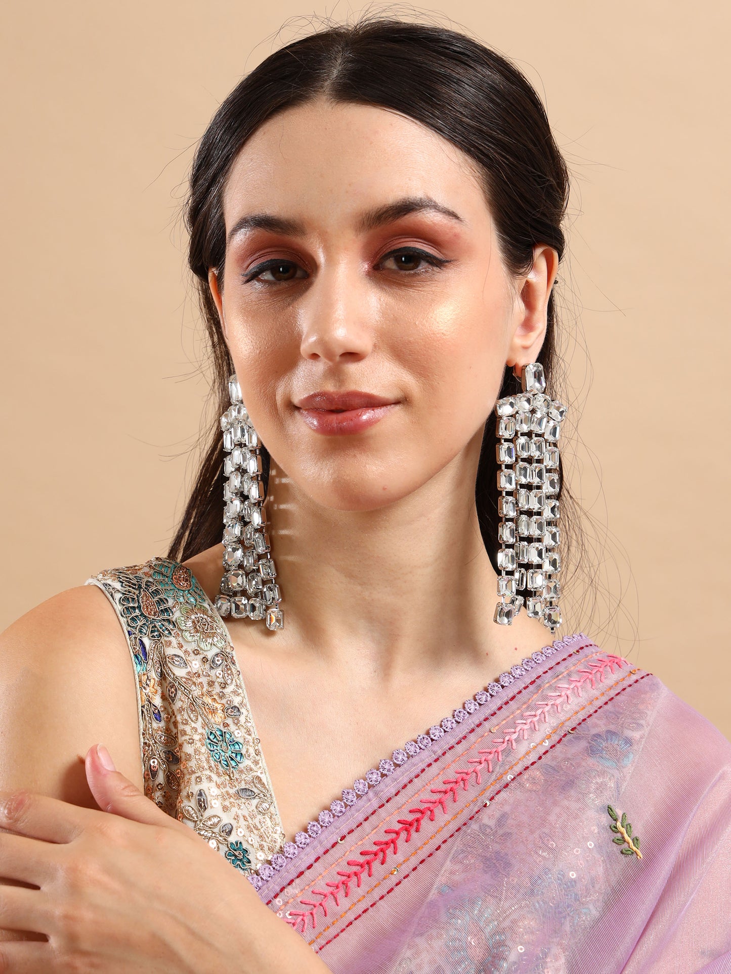 A woman wearing Long Rhinestone Tassel Earrings poses gently against a beige background, dressed in a pink embroidered saree and smiling with her hand resting on her shoulder.