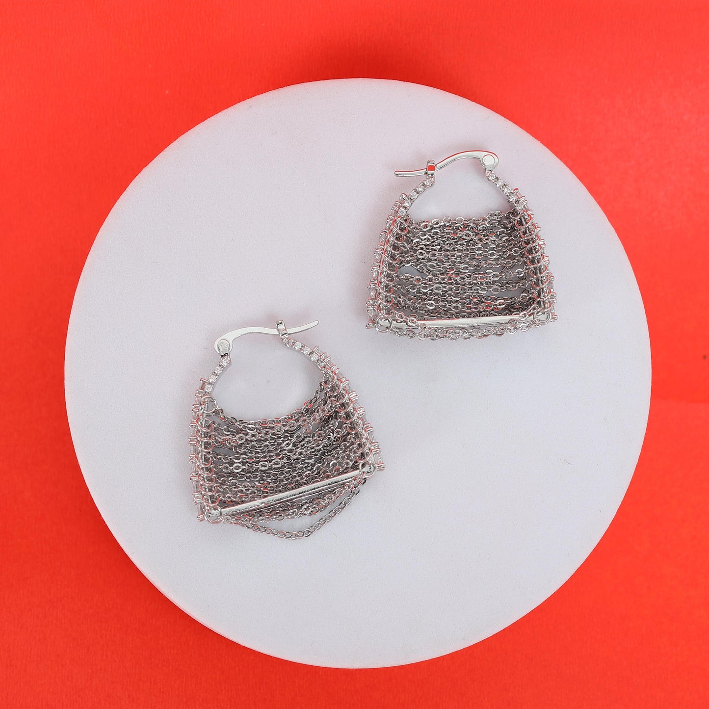 A pair of Silver Chain Bag Earrings featuring a rectangular bar detail are displayed on a round white surface with a bright red background—perfect for storing in your lightweight jewelry pouch.