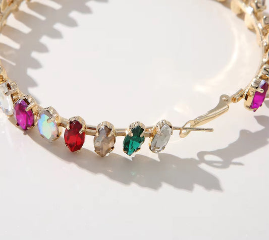 A close-up of the Big Multicolour Hoops, featuring oval-cut red, green, purple, blue, and clear gemstones in prong settings on 18K gold-plated hoops for an affordable touch of luxury against a light background.
